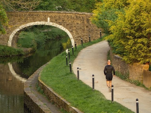 A Lone Runner Exercises along the Tow Path of the Leeds and Liverpool Canal at Dowley Gap near Hirst Wood, Shipley, Yorkshire Caught in the Rays of the Setting Sun
