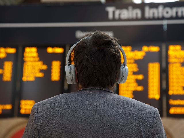 Person with headphones looks at train time board